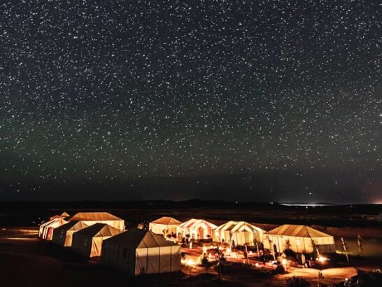 Desert camp tents lit up under a starry night sky