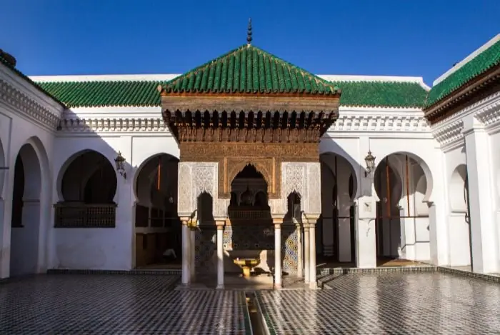 The courtyard of the Al Attarine Madrasa in Fes, with its carved cedar canopy and green-tiled roof